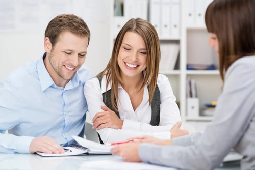 Investment adviser giving a presentation to a friendly smiling young couple seated at her desk in the office Investment adviser giving a presentation to a friendly smiling young couple seated at her desk in the office
